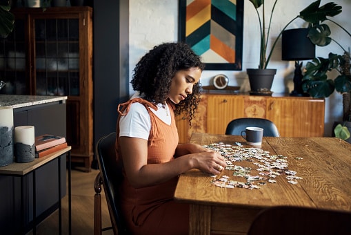 Woman doing a jigsaw puzzle to stay sharp on the dining room table in a trendy home. 