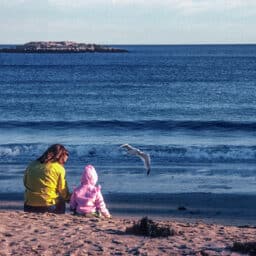 Mother and child sitting on the beach watching the waves and seagulls.